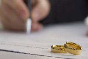 Individual signing a document with wedding bands in front of them